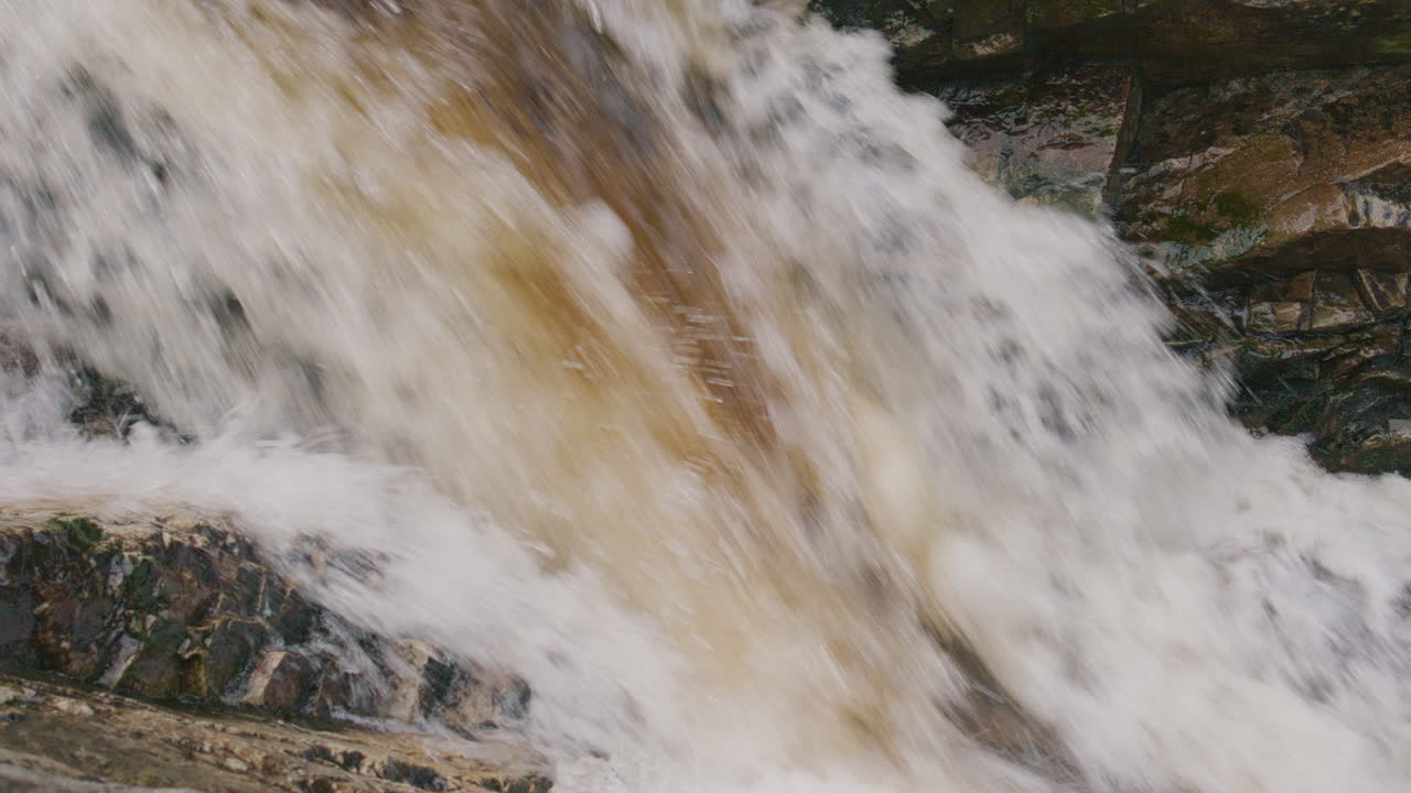 Close-up view of foaming water cascading powerfully over mossy rocks in a forest stream, conveying raw energy and the relentless momentum of nature's elemental force.