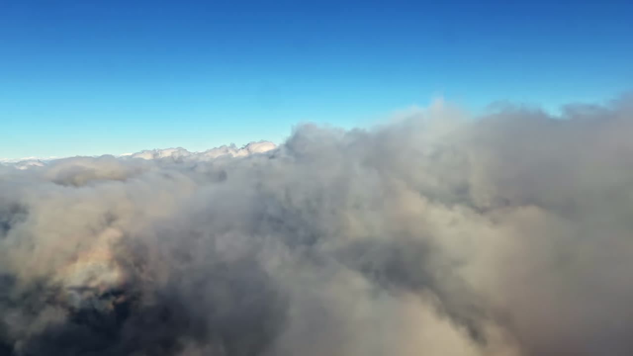 Aerial view of clouds covering mountaintops under clear blue sky, high altitude