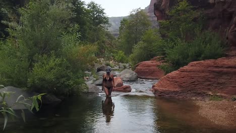 model in bikini, slow motion walking out of running water river surrounded by rocks and trees