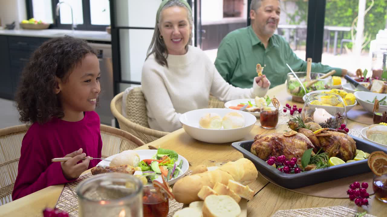 Diverse family dining at table, mother offering roll, child eating salad, dad eating turkey