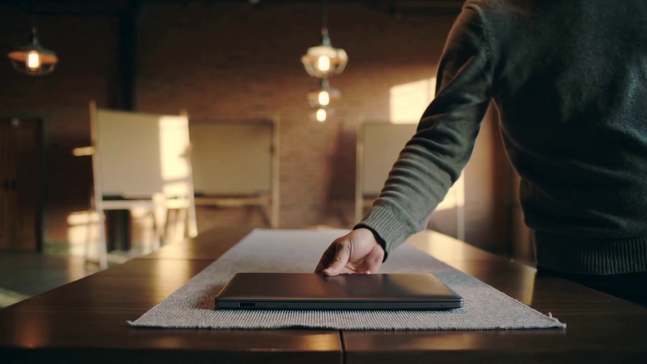 Ein Mann in olivfarbenem Pullover betritt ein Loft, legt einen Laptop auf einen Läufer, bereitet sich vor, tritt zurück, mit Platz für Text.