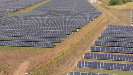 Aerial-close-up-fly-over-view-of-large-solar-farm-with-many-rows-of-solar-panels-creating-green,-renewable-energy-to-replace-fossil-fuels-and-to-power-clean-transition-to-fight-climate-change