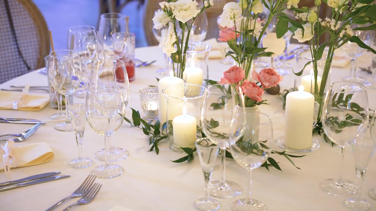 Tavolo da ricevimento nuziale romantico splendidamente decorato con candele luminose, centrotavola floreali, bicchieri di cristallo ed eleganti coperti in un'illuminazione ambientale calda e soffusa. Nessuno visibile