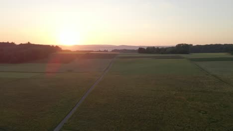 side-flying aerial footage at sunset over meadows and fields surrounded by beautiful large forests and hills in the background