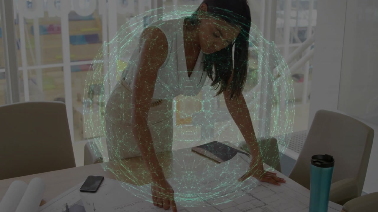 Woman leaning over table reviewing documents with smartphone, showing animated finance graph