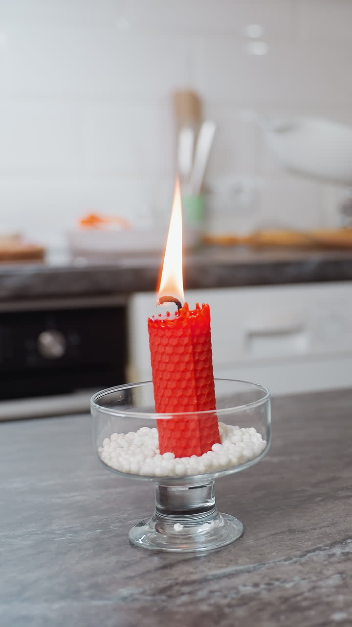 vista parcial de una mujer colocando un cuenco blanco en la mesa de la cocina mientras sostiene huevos en la mano adornados con una pulsera, una vela roja ardiente y una taza de vidrio de azúcar en la mesa