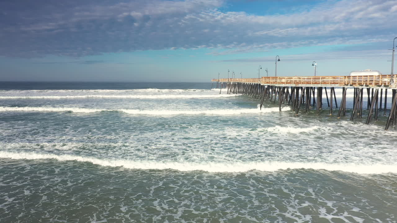 olas rodando hacia la playa junto al emblemático muelle de pismo beach - retroceso aéreo