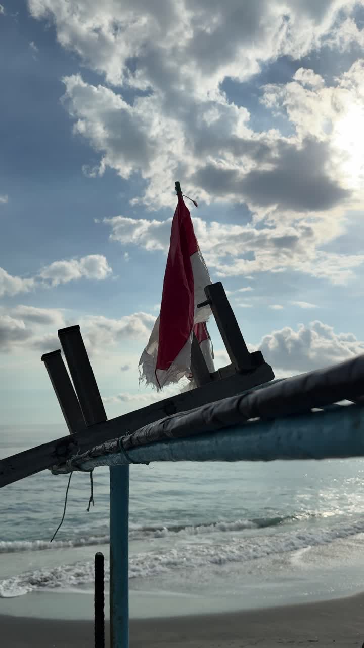 Bandiera indonesiana logora che ondeggia delicatamente su una spiaggia con le onde dell'oceano