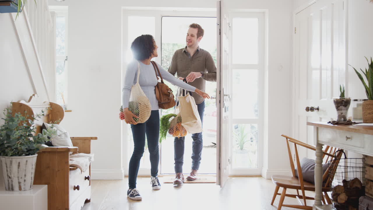 pareja que regresa a casa de un viaje de compras llevando comestibles en bolsas de plástico
