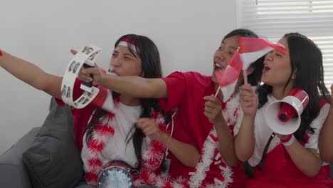 young indonesian football supporters holding megaphone and tambourine, recording video on smartphone to celebrating their team winning