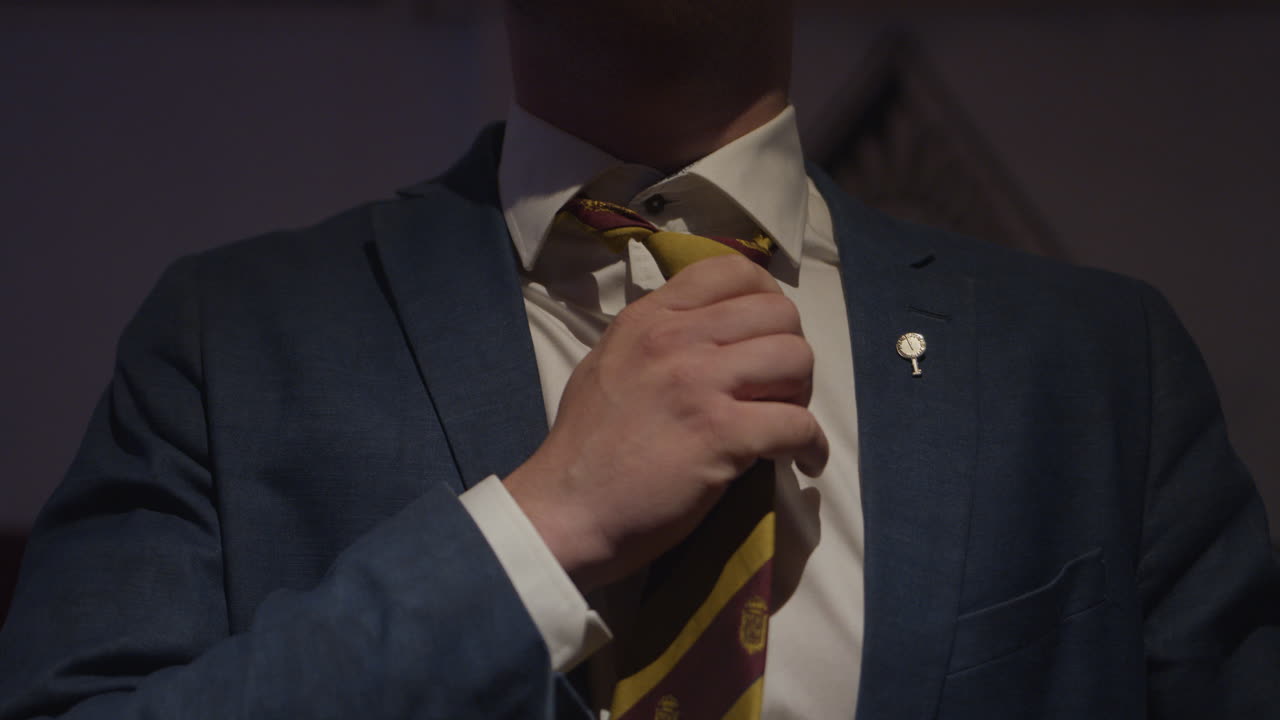 un hombre con un traje azul oscuro apretando su corbata despojada