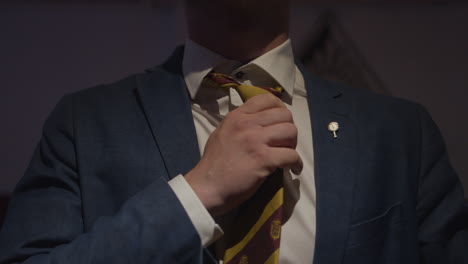 a man wearing a dark blue suit tightening his stripped tie