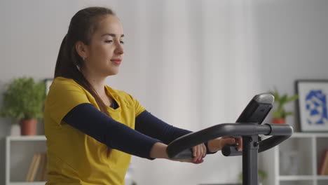 Una-Joven-Tranquila-Está-Haciendo-Ejercicio-Con-Una-Bicicleta-Estática-En-Casa,-Una-Actividad-Deportiva-Y-Un-Estilo-De-Vida-Saludable,-Retrato-Medio-De-Una-Deportista-En-Casa