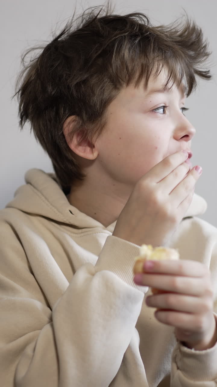 Calm brunet teenager eating a tangerine. Boy with messy hair eats fruit looking around and then into camera. Vertical video