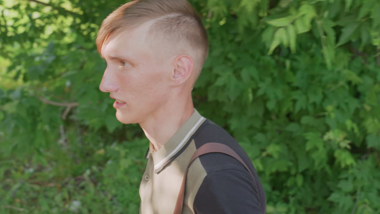 Anxious Youth Adjusting Backpack, Caucasian Male Displaying Nervous Gestures Outdoors, Young Individual Of Caucasian Descent Showing Signs Of Anxiety Near Foliage While Fiddling With Backpack