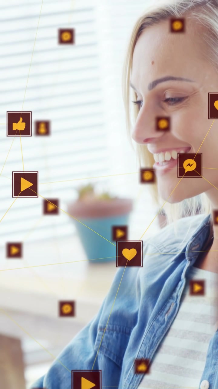 Vertical video: Woman browsing device by window animating social icons drifting past face smiling