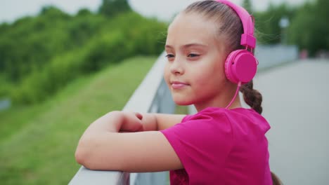 a young girl enjoying a peaceful moment outdoors while listening to music through bright pink headphones, showcasing her relaxed demeanor and love for sound in a beautiful green setting