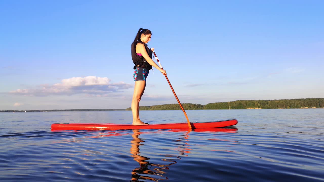 There is young girl paddle boarding in the big lake