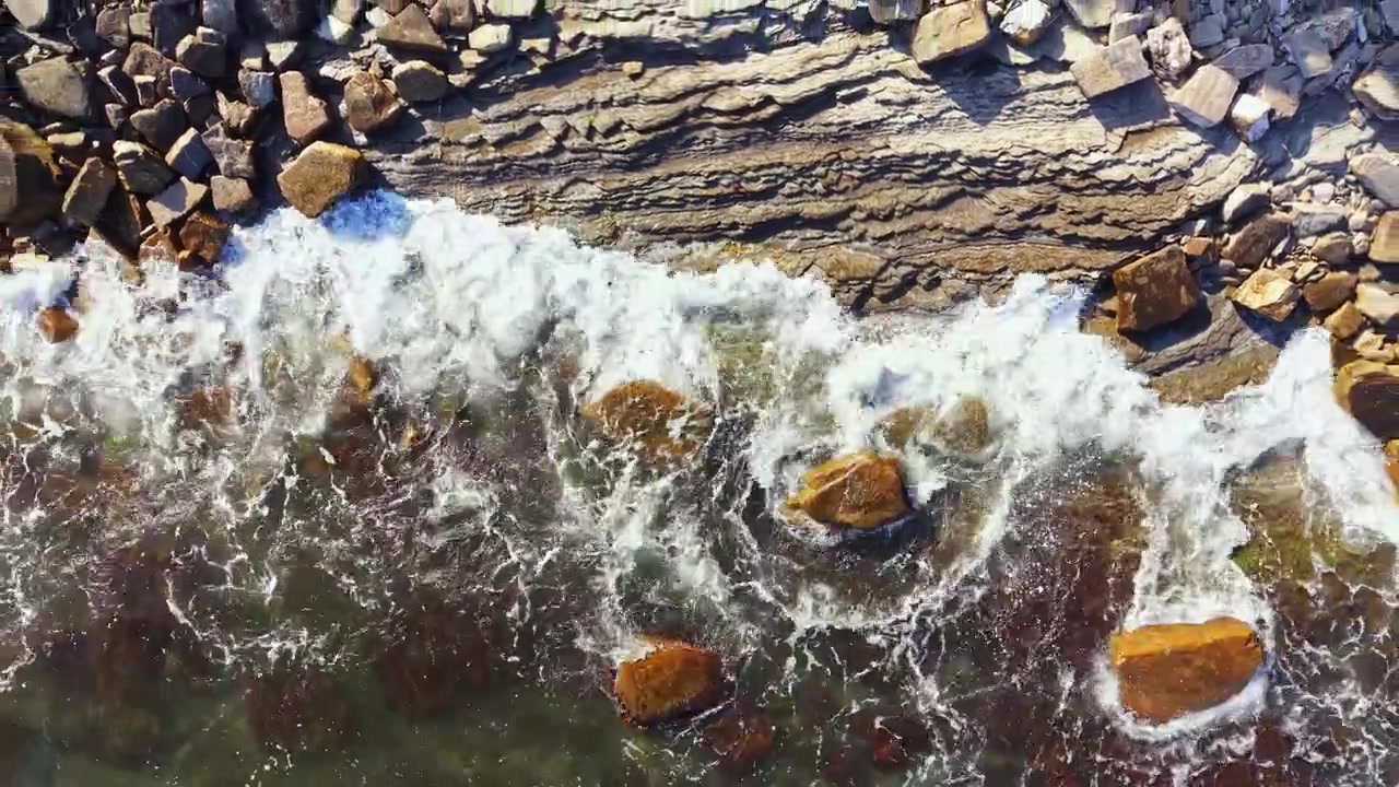 Le onde si infrangono sulle rocce lungo la costa mentre la marea sale su una spiaggia durante le ore diurne