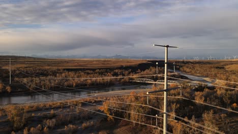 drone flying backwards through power lines in southern alberta, canada. close call with electricity poles. cinematic aerial footage of beautiful old bridge in the outskirts of the rocky mountains.