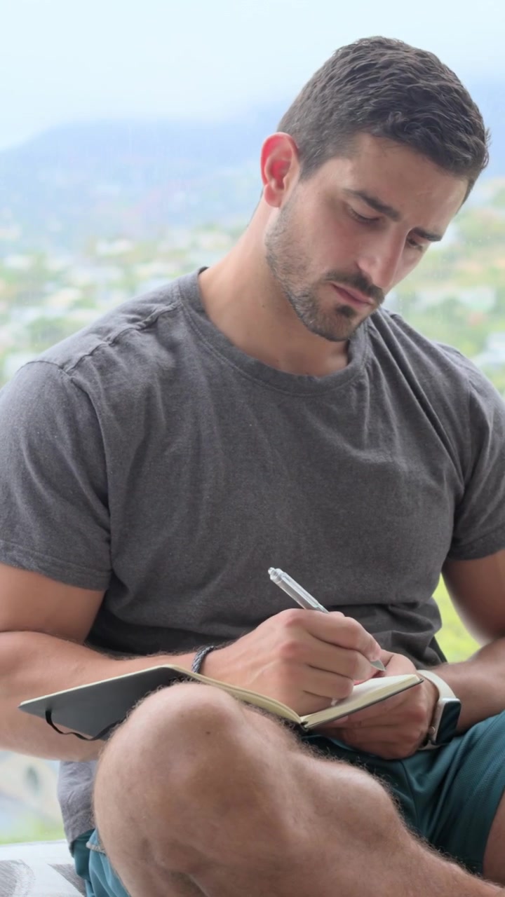 Vertical video: Placing hands on chest man in tee centering breath on patio picking journal writing