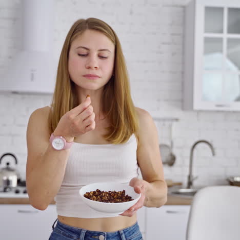 pretty woman eats nuts at home. portrait of a beautiful female in the modern kitchen. slim girl enjoys eating natural food. healthy food concept.