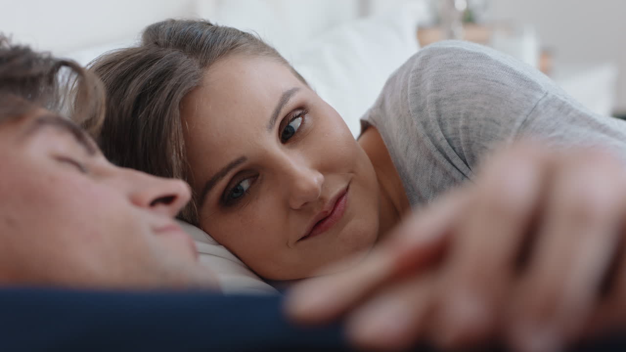 pareja joven feliz acostada en la cama compartiendo una relación romántica mujer hermosa sosteniendo la mano de su esposo disfrutando de la intimidad con su pareja relajándose juntos en casa imágenes 4k