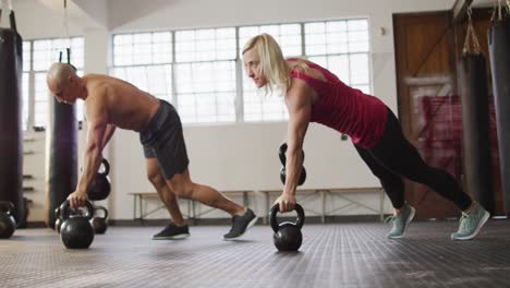 mujer y hombre caucásicos en forma trabajando con campanas en el gimnasio