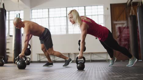 fit caucasian woman and man working out with kettle bells at the gym