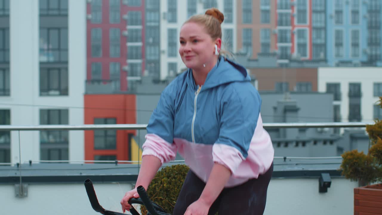 Athletic woman riding on spinning stationary bike training routine on house rooftop weight loss