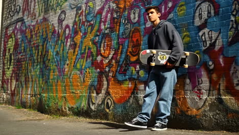 young skateboarder standing by a graffiti wall