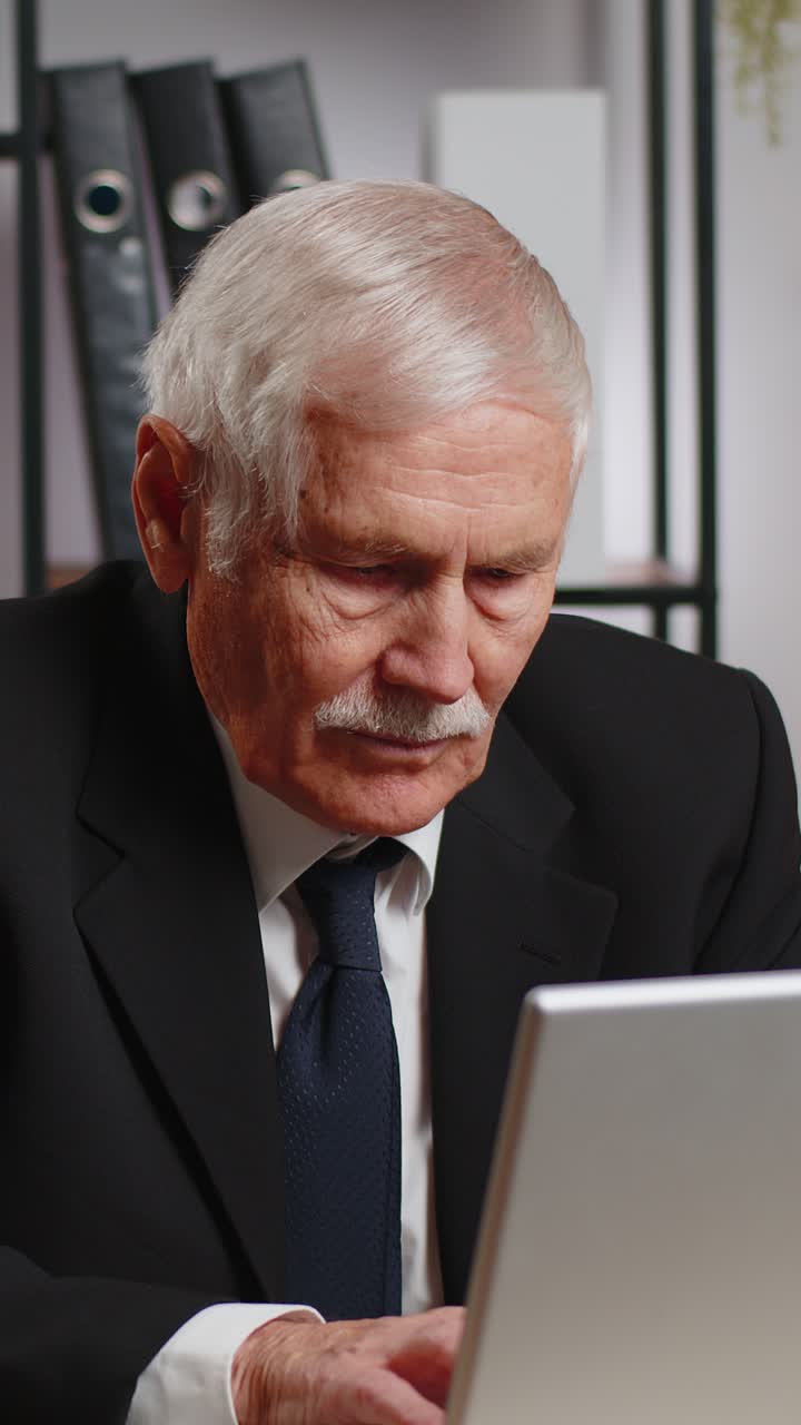 Nonno caucasico, uomo d'affari, seduto alla scrivania dell'ufficio di casa che chiude il PC portatile dopo aver finito di lavorare