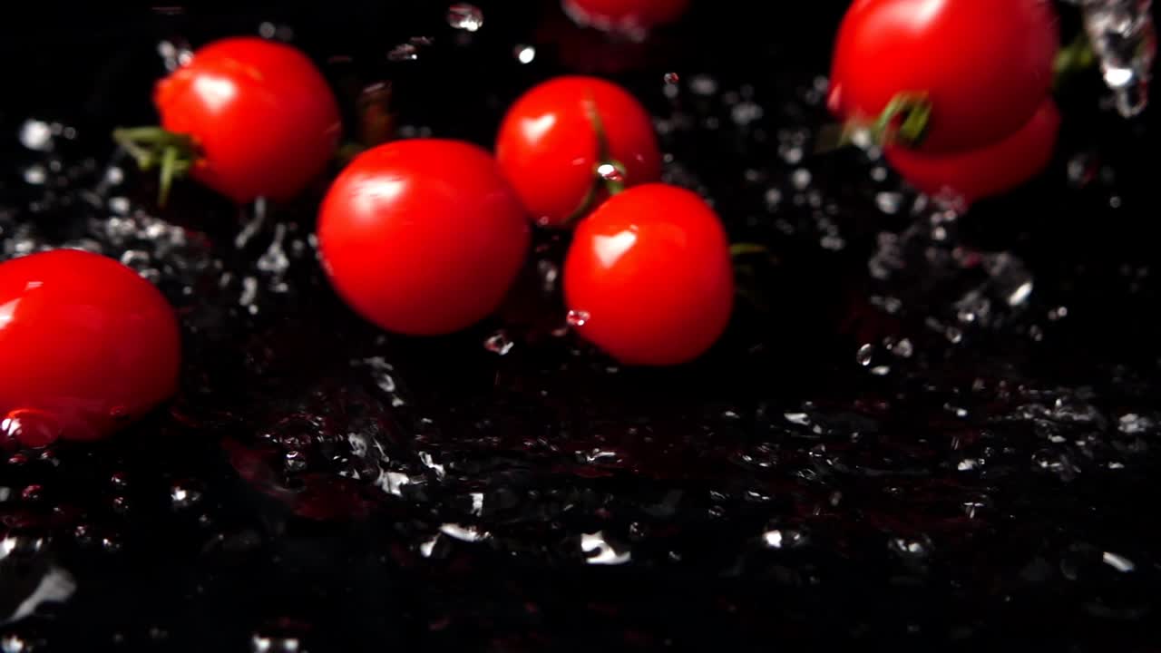 The falling cherry tomatoes in water on a black background. Slow motion