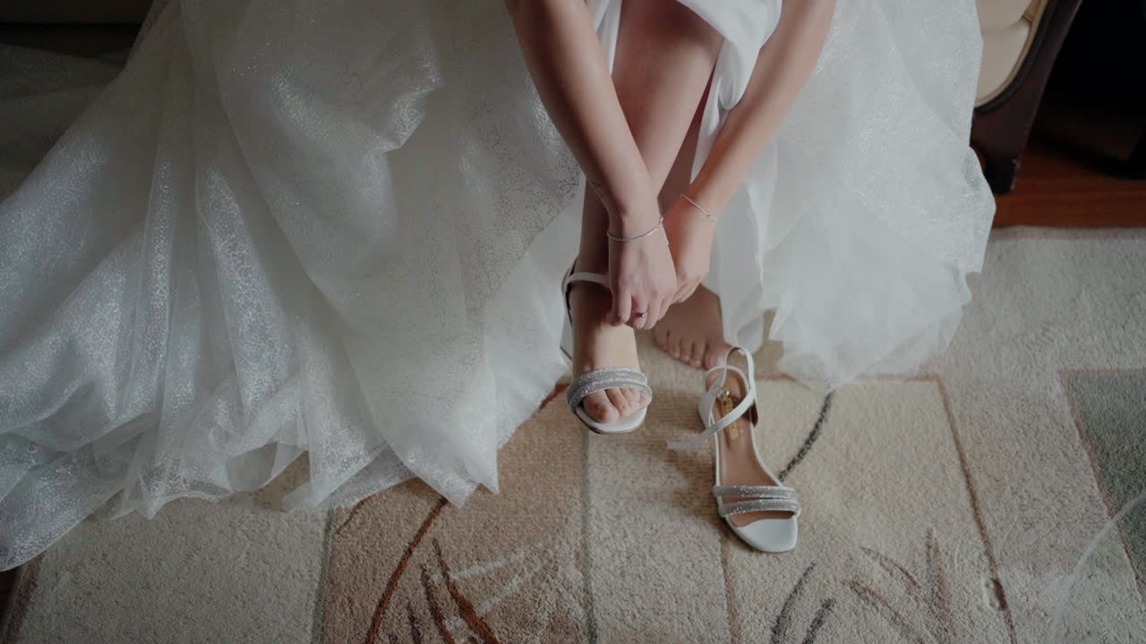 Bride adjusting her wedding shoes, with her dress spread out around her, sitting on a carpet