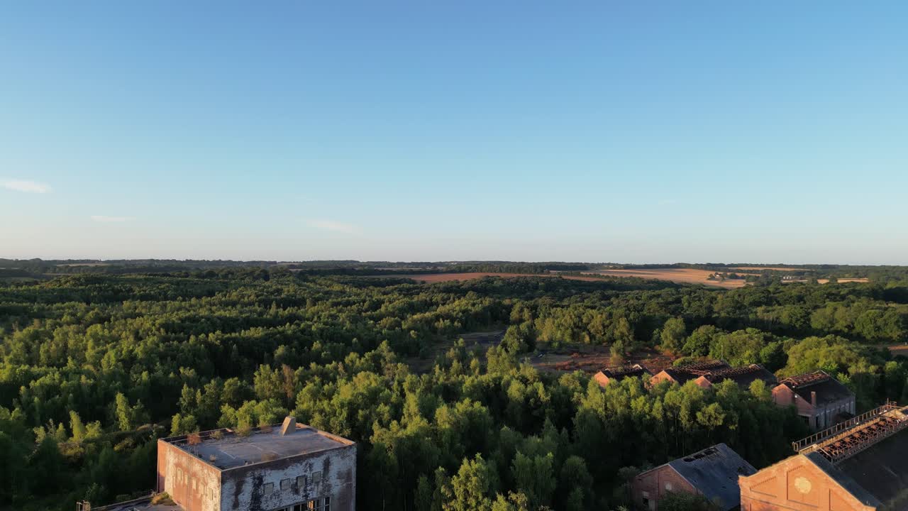 Drone rising from a disused coal mining complex for a view of a forest