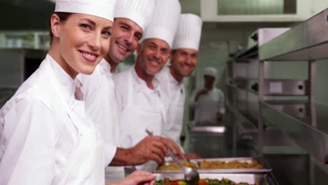 Fila-De-Chefs-Preparando-Comida-En-Bandejas-Para-Servir.