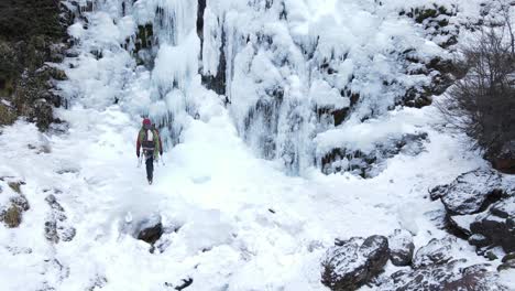 climber man with backpack walking towards a frozen waterfall