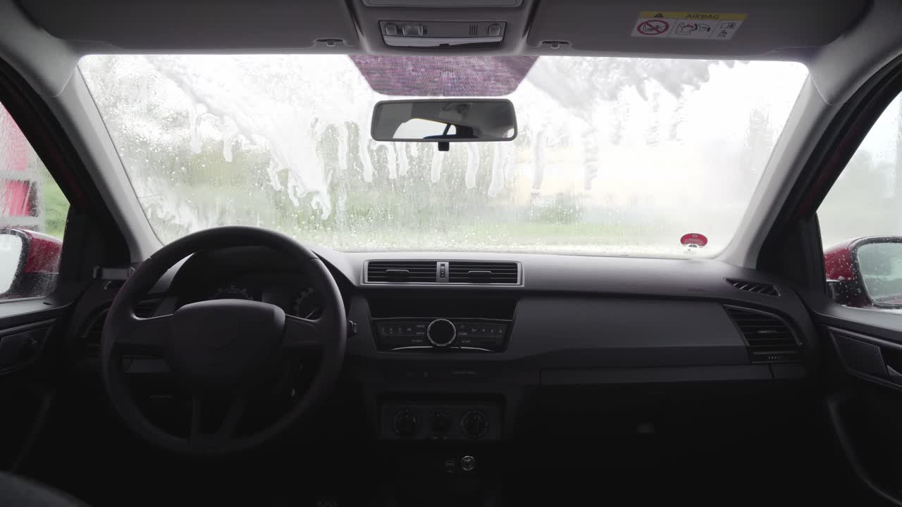 White foam on windscreen during car wash, interior view, man in background