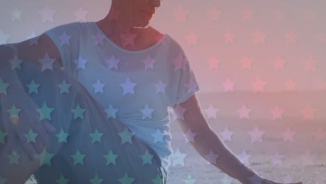Animation-of-american-flag-pattern-over-senior-woman-sitting-on-beach