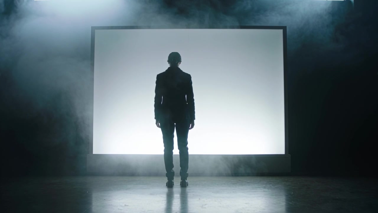 Walking man wearing fitted jacket and pants moving toward backlit screen pulling him in studio fog