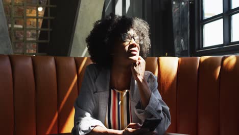 Mujer-Afroamericana-Sentada-En-Un-Café-Mirando-La-Ventana-Y-Sonriendo