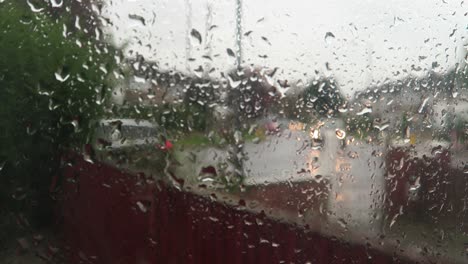 Lluvia-Cayendo-En-La-Ventana-Con-Un-Fondo-Borroso-De-Tráfico-Fuera-De-La-Calle-Pasando