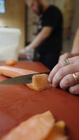 close up vertical view of knife cut salmon slice and hand put away piece