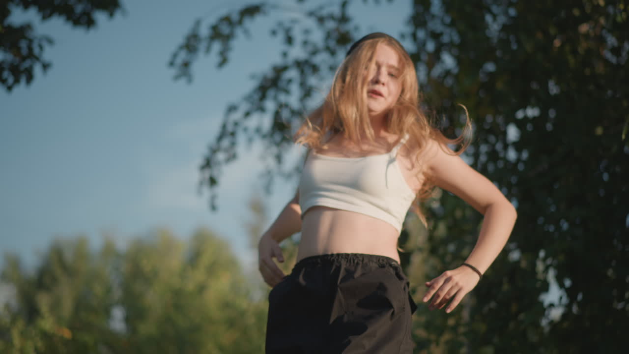 Ballerino urbano dinamico esegue mosse espressive, prova intensa di freestyle in un parco, gesti concentrati e movimenti di capelli, ritmo hip-hop ad alta energia, sneakers e abbigliamento streetwear, creazione di contenuti e allenamento