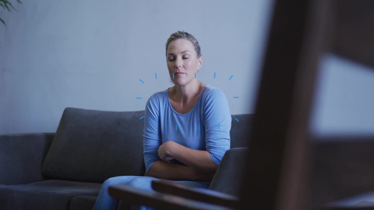 Sitting on sofa, woman in blue shirt appearing thoughtful and relaxed