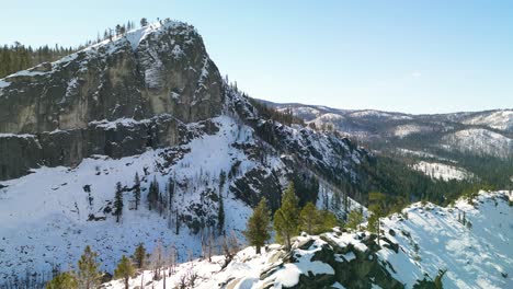 Aerial-view-of-mountain-top-with-distant-large-rock-wall,-Lake-Tahoe,-California-winter