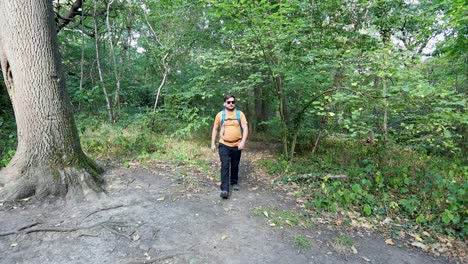 un joven con una mochila y gafas de sol sale del bosque y comprueba la brújula de su teléfono