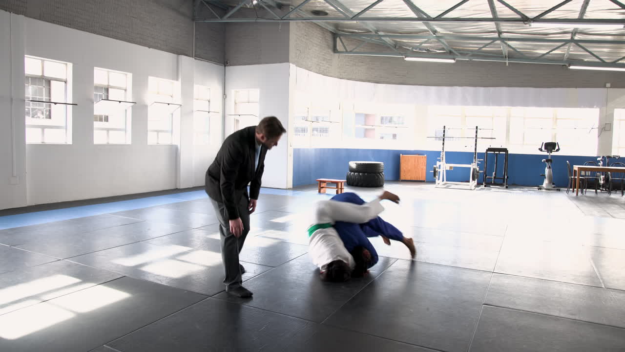 Practicing judo, two people sparring on mats in gym, focusing on technique