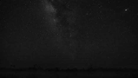 milky way time lapse at night by a lake with silhouette of trees