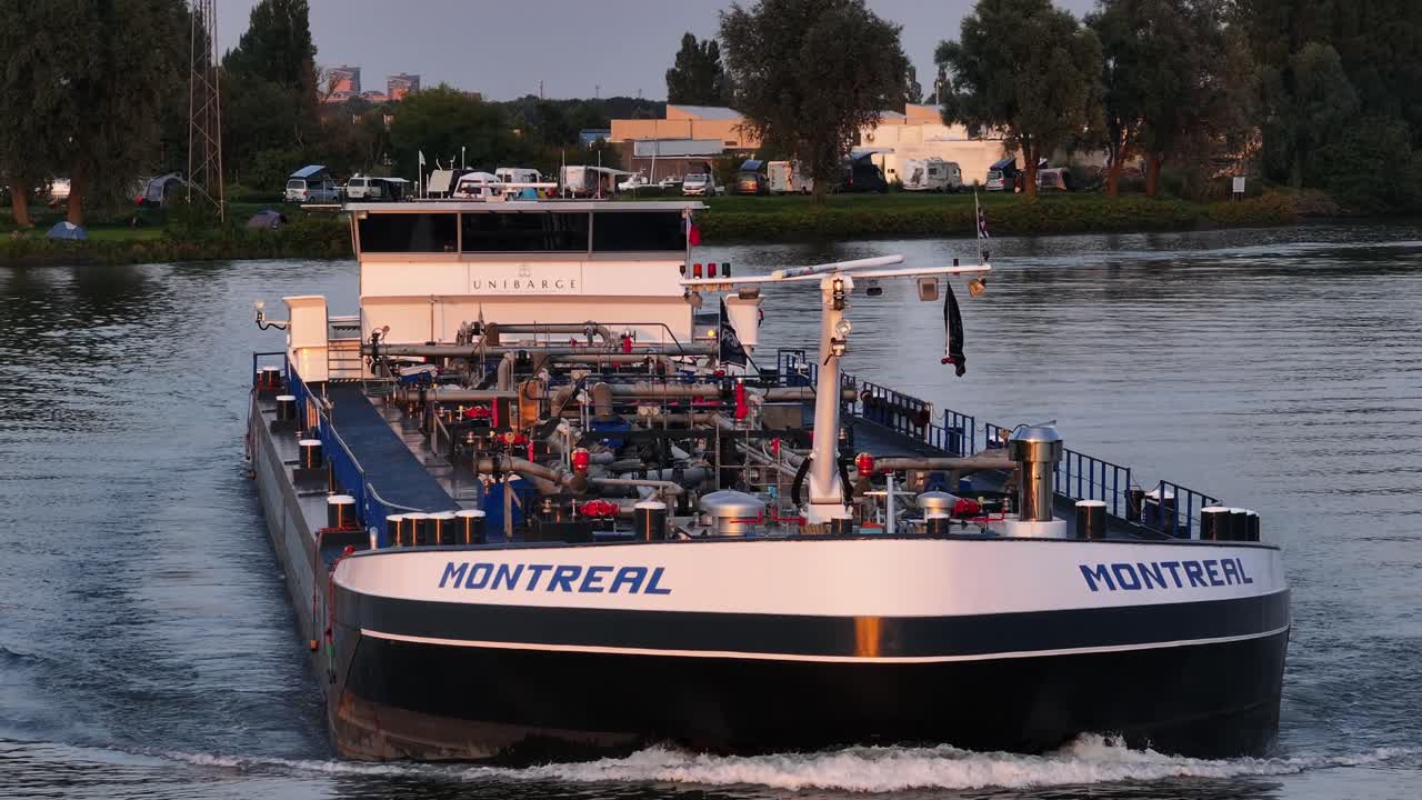 A large cargo ship named "Montreal" sails calmly on a river during sunset